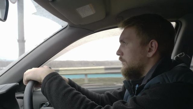 Bearded young man driving a car. Serious and attentive driver in the city