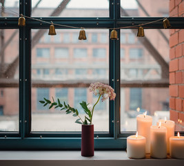 Kerzen im Fenter mit weihnachtlicher Dekoration und Blumen