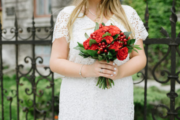Hands of the bride hold a bouquet of red flowers