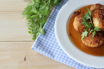 Sweet and sour eggs in white dish with coriander on wooden table.