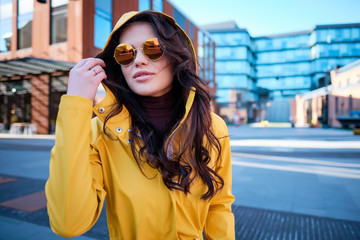 Attractive hipster young woman in stylish sunglasses in a stylish yellow coat