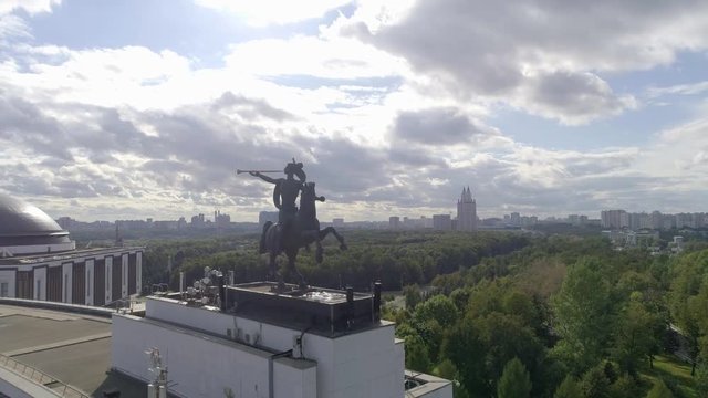 Shooting a building on the roof of which is a sculpture rider on a horse trumpets in a pipe, against the city Park and the city, aerial photography Sunny day and good weather