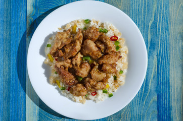 chicken in sweet and sour sauce and rice with vegetables on white plate blue background