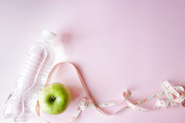 Diet symbol flat lay one meter ribbon and green apple and a bottle of water. pink background with...