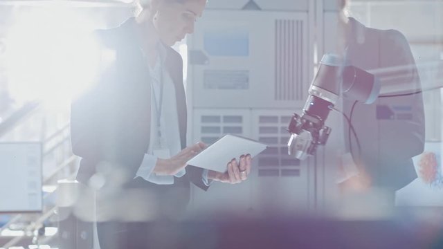 Stylish Female Industrial Robotics Engineer Uses Tablet Computer to Program and Manipulate Robot Arm for Lifting, Moving Objects. Technology Research Facility for Machine Learning and Cloud Computing