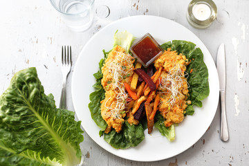 Colorful baked french fries with vegetables. with vegetable stew on iceberg lettuce.