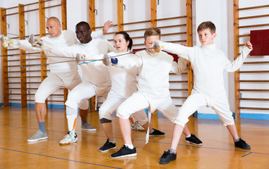 Coaches demonstrating to young athletes attack movements with rapier during fencing workout