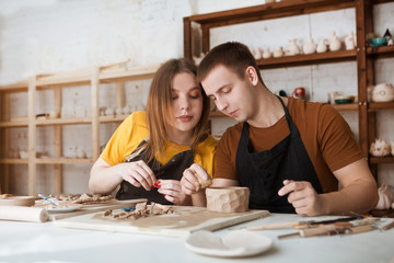 couple in casual clothes and aprons making ceramic pot on pottery at table in workshop