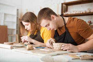 couple in casual clothes and aprons making ceramic pot on pottery at table in workshop