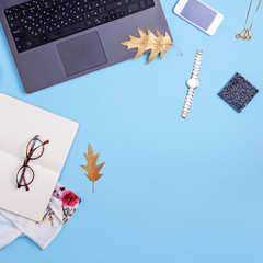 Home office workspace with laptop, glasses and dress on blue background. Fashion blogger work concept