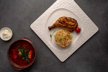 half an appetizing grilled chicken with rice and cherry tomato on white plate, on dark table, horizontal top