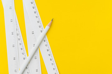 Pencil and white measuring tapes with centimetre and inches on vivid yellow background, length,...