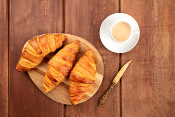 A photo of croissants with coffee and a vintage knife, shot from above on a dark rustic wooden background with a place for text