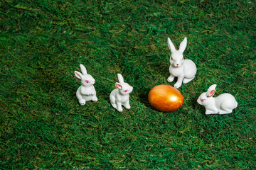 Happy Easter. Congratulatory easter background. Little white bunnies around golden egg on a background of moss. Space for text