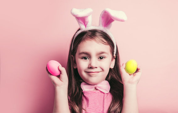 Cute little girl with bunny ears on pink background. Easter child portrait, funny emotions, surprise. Copyspace for text.