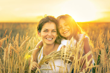 Young woman and her daughter on golden wheat field at sunny summer evening. © sborisov