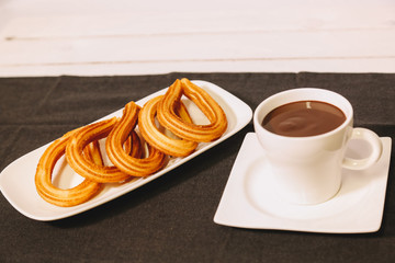 spanish fritters served on a wooden table with a gray tablecloth and a cup of hot chocolate
