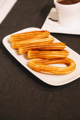 spanish fritters served on a wooden table with a gray tablecloth and a cup of hot chocolate