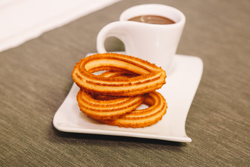 spanish fritters served on a wooden table with a gray tablecloth and a cup of hot chocolate
