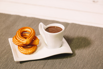 spanish fritters served on a wooden table with a gray tablecloth and a cup of hot chocolate