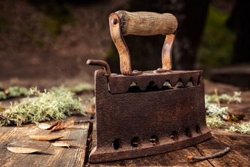 Close up of an antique and rusty iron from coal ironing with wooden handle, on an antique wooden table. Houseworks. Vintage laundry.