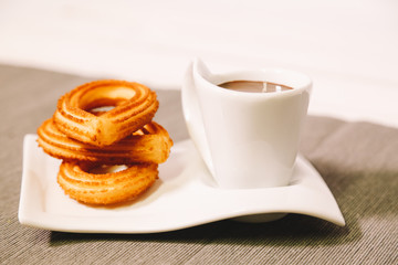 spanish fritters served on a wooden table with a gray tablecloth and a cup of hot chocolate