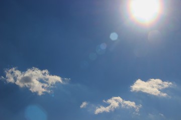 A ray of golden sun against a bright blue sky with small clouds