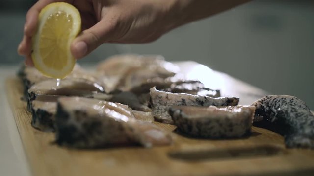 Female hands pouring fish fillet with lemon juice on wooden tablet. 4K