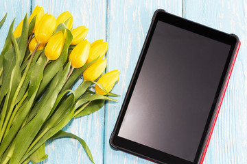 mother's Day concept. tulips flower on pastel blue wooden background, Next to the tablet computer with space for text.