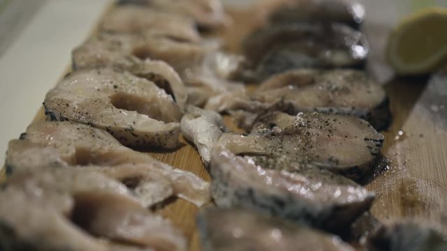 Female hands strewing spices on fish fillet on wooden tablet. 4K