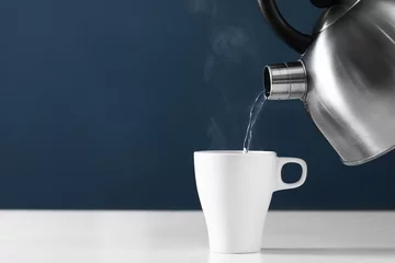 Poster Gießen Sie heißes Wasser in eine Tasse auf dunklem Hintergrund. Tasse Tee mit Dampf. Metallkessel © Andriy Medvediuk