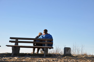 Paar auf einer Parkbank am Aussichtspunkt vor blauem Himmel 