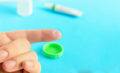 Contact lens on finger on light blue background.Eye care products in the background, space for text ,top view.