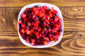 Traditional russian salad vinaigrette with beetroot, carrot, potato, onion and pickled cucumbers on wooden table. Top view