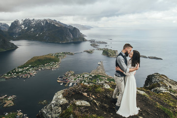 Fototapeta na wymiar Wedding couple travelers on a hill in Norway, Kvalvika. Beautiful view of the beach, Lofoten, Norway.