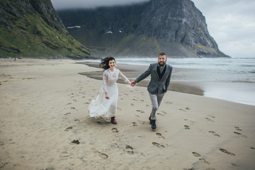 Wedding couple travelers on a hill in Norway, Kvalvika. Beautiful view of the beach, Lofoten, Norway.