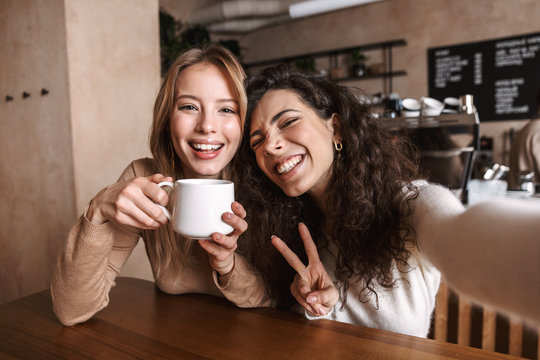 Excited happy pretty girls friends sitting in cafe take a selfie by camera. - Powered by Adobe