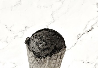 black ice cream with activated charcoal in a black waffle cone against a background of white marble. copy space. top view. coconut charcoal