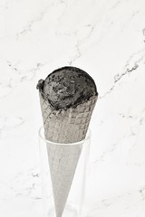 black ice cream with activated charcoal in a black waffle cone against a background of white marble. copy space. top view. coconut charcoal