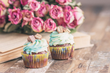 Handmade chocolate muffins with decorations. Book and a bouquet of roses, blurred background