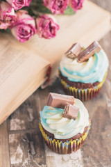 Handmade chocolate muffins with decorations. Book and a bouquet of roses, blurred background