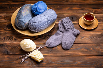 gray knitted socks, knitted yarns and a cup of tea on a saucer on a wooden background