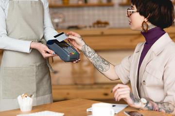 partial view of waitress holding payment terminal near businesswoman with credit card
