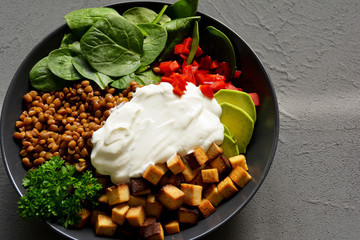 Bowl mit Linsen, Tofu, Spinat, Paprika, Avocado, Joghurt und Petersilie