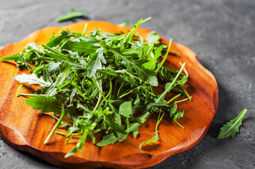 Fresh green arugula leaves in a wooden plate on Dark grey black slate background with copy space. top view