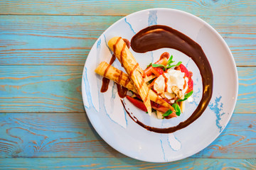 Top view delicious dessert with waffle rolls, ice cream and strawberries