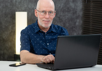 senior man with beard and blue shirt in the office using laptop