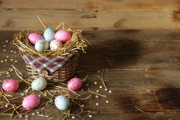 Fototapeta na wymiar Easter eggs in a basket decorated with straw on a wooden rustic background with copy space for text. Easter Postcard.