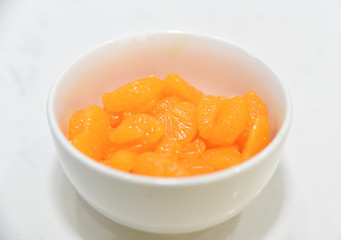 Sliced oranges in the white bowl on the white stone table.