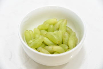 Fresh green grape in the white bowl on the white stone table.